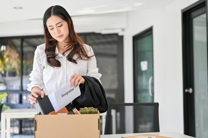 Sad Asian female office worker packing her stuff into a cardboard box in the office, quitting her job